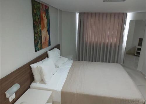 a bedroom with a white bed and a window at Confortável flat em frente à praia de Tambaú in João Pessoa