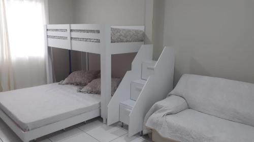 a white bedroom with a bunk bed and a chair at Espaço de praia acolhedor para família e pets in Matinhos