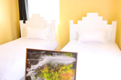 twee bedden met witte kussens en een foto in een kamer bij jenna stays in Nyeri