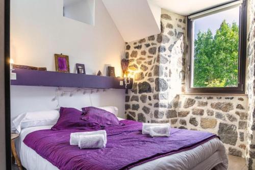 a bedroom with a purple bed with a stone wall at Lo d Ici, Gite de groupe et de Caractere in Nasbinals