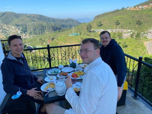 un grupo de tres hombres sentados en una mesa comiendo comida. en House of Leisure, en Nuwara Eliya