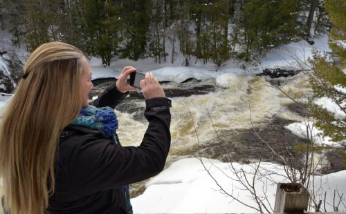 a woman taking a picture of a river in the snow at Chalet Du Marais in Saint-Paulin
