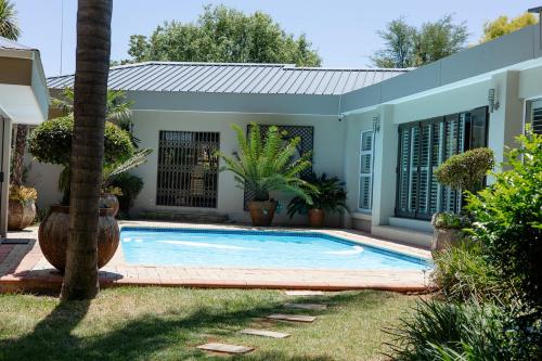 a swimming pool in front of a house with plants at Tristan's Place Guest House in Klerksdorp