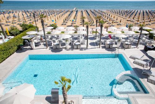 una piscina con sillas y sombrillas y una playa en Hotel Sayonara, en Lido di Jesolo