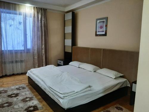 1 dormitorio con 1 cama con sábanas blancas y ventana en Гостевой дом Almatau House, en Besqaynar