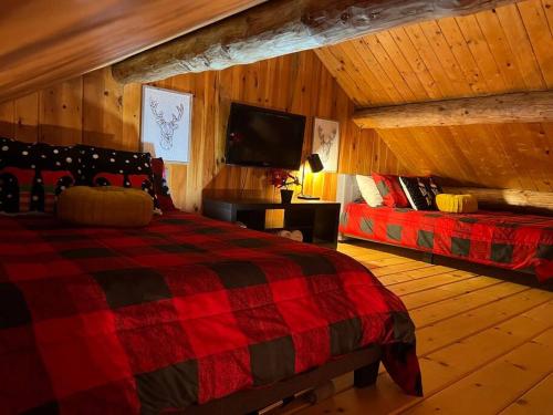 a bedroom with a red and black bed and a tv at Chalets Terre De l’Orme with Spa tucked away in nature in Saint-Gabriel-De-Valcartier