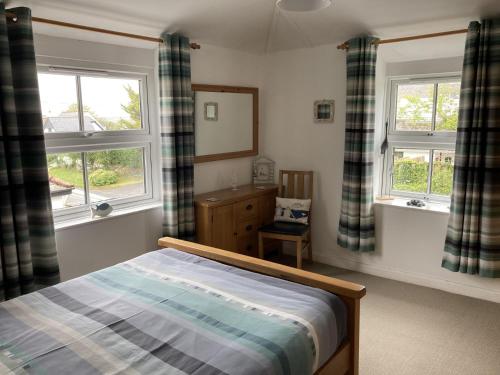a bedroom with a bed and two windows at Hollyhocks in Saint Minver