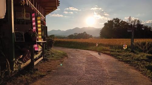 a dirt road next to a field with the sun in the sky at Chill In Pai - ชิลล์ อิน ปาย in Pai