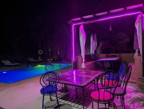 - une table et des chaises à côté d'une piscine avec des lumières violettes dans l'établissement villa sophie, à El Jemʼa Ghemat