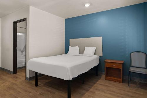 a bedroom with a white bed and a blue wall at WoodSpring Suites Champaign near University in Champaign