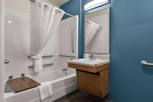 a bathroom with a sink and a tub and a mirror at WoodSpring Suites Champaign near University in Champaign