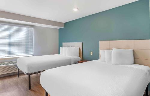 two beds in a room with blue walls and a window at Extended Stay America Select Suites - Little Rock - Southwest in Little Rock