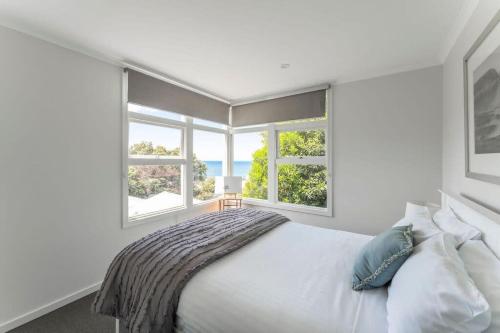 a white bedroom with a bed and two windows at Cosy Unit With a Sea View in Burnie