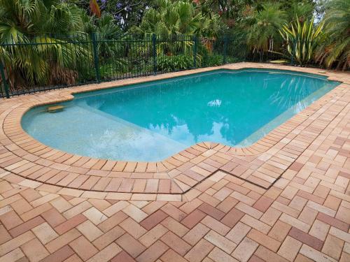 a swimming pool with a brick floor and a brickkered swimming pool at Tranquil Garden Hideaway in Ormeau