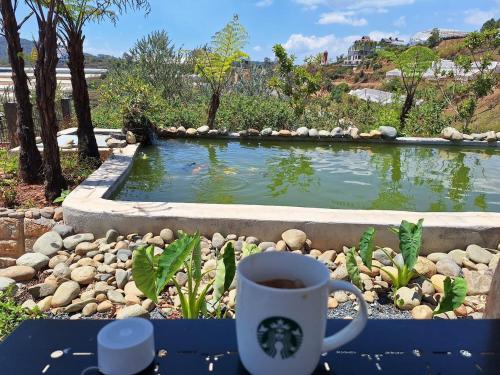 a cup of coffee sitting on a table in front of a pond at Windy Home in Ấp Man Ling