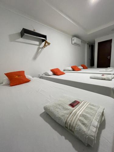 Habitación con 3 camas blancas con almohadas de color naranja. en Hotel Pousada Acauã Acesso através de escadas en Campina Grande