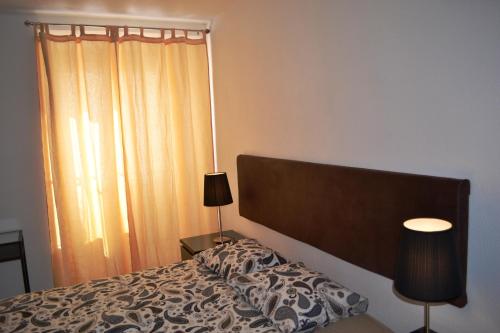 ein Schlafzimmer mit einem Bett, zwei Lampen und einem Fenster in der Unterkunft Andar com jardim e estacionamento in Paço de Arcos