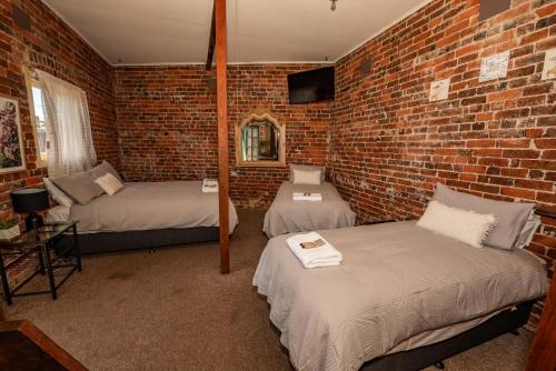 a room with two beds and a brick wall at The Centennial Hotel Gulgong in Gulgong