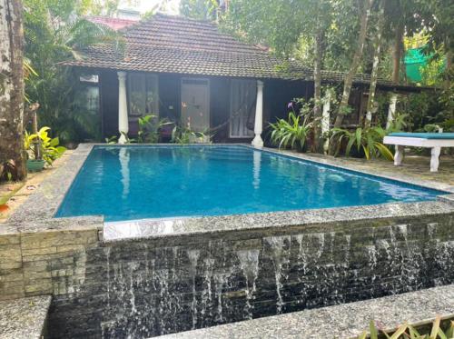 a swimming pool with a waterfall in front of a house at Marari Dreamz Homestay in Mararikulam
