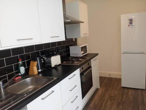 una cucina con armadi bianchi, lavandino e frigorifero di Double bed (R1) close to Burnley city centre a Burnley