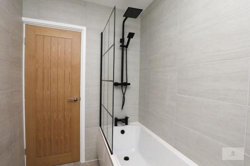La salle de bains est pourvue d'une baignoire et d'une porte en bois. dans l'établissement Newly Renovated 3 Bedroom House with Parking by Amazing Spaces Relocations Ltd, à Liverpool