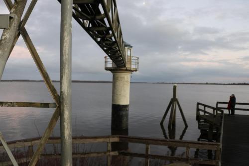 a person standing on a dock next to the water at Urlaubsruhe 6 Pers Holiday home w terrace close to National Park Lauwersmeer in Anjum