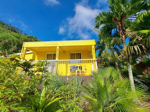 a yellow house with a white porch and palm trees at Bungalow Jazz - Bassin Manapany-Les-Bains in Saint-Joseph