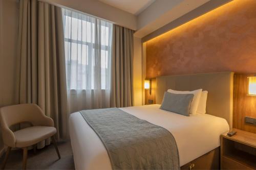 una camera d'albergo con un letto, una sedia e una finestra di Riu Plaza The Gresham Dublin a Dublino