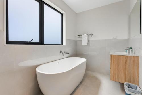 a white bathroom with a tub and a sink at Sleek Vista Townhouse with deck and air-con in Auckland