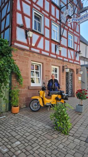 a man sitting on a yellow motorcycle in front of a building at Brunnenputzer Pension Restaurant in Külsheim