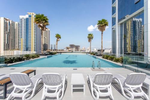 a swimming pool on the roof of a building with chairs and palm trees at Holiday Studio In JVC 2302, Dubai in Dubai