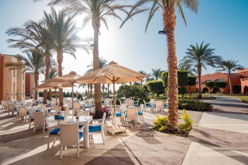 un restaurante con sillas, sombrillas y palmeras en Novotel Marsa Alam Beach Resort en Quseir
