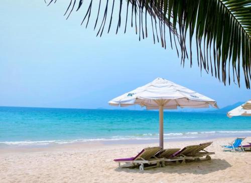 a beach with two lounge chairs and an umbrella at TTC Van Phong Bay Resort in Ninh Hòa