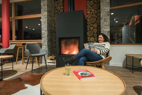a woman sitting in a chair reading a book in front of a fireplace at Belambra Clubs Les Saisies - Les Embrunes - Ski pass included in Villard-sur-Doron
