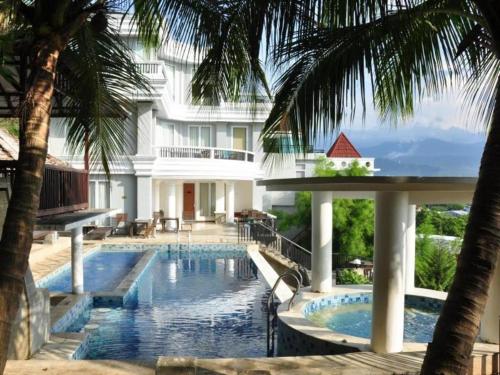 a swimming pool in front of a building with palm trees at Hotel Minahasa in Manado