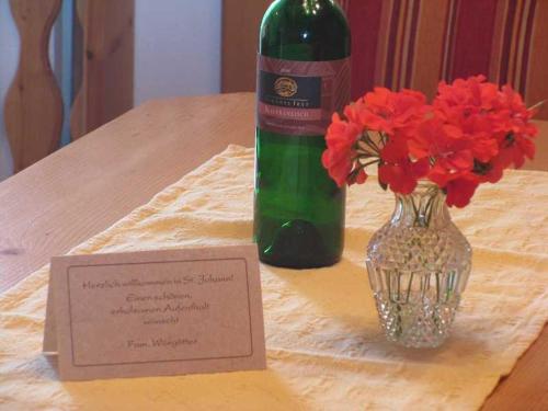 una botella de vino sentada junto a un jarrón de flores rojas en Appartements Wörgötter Astrid & Sepp en Rettenbach
