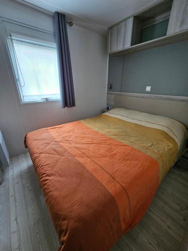 une chambre avec un grand lit avec une couverture orange dans l'établissement Grand Mobil Home A114, à Saint-Jean-de-Monts