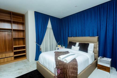 Un dormitorio con una cama grande con cortinas azules. en ELEGANT DUPLEX @ Rosedale Apartments, en Accra