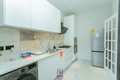 Una cocina blanca con fregadero y refrigerador. en ELEGANT DUPLEX @ Rosedale Apartments, en Accra