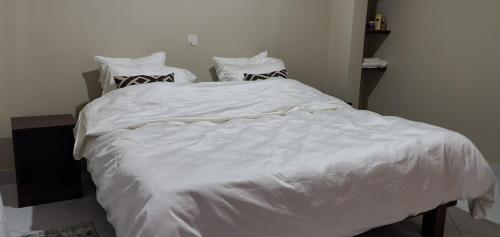 ein weißes Bett mit weißer Bettwäsche und Kissen in der Unterkunft Orchard Residence Arusha in Arusha