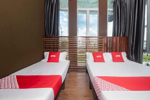 two beds with red pillows in a room with windows at Hotel O Hi Inn 3 in Sibu