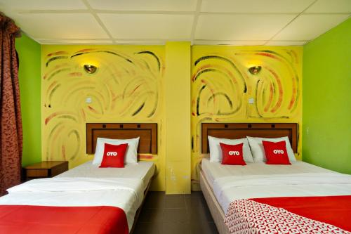 2 camas en una habitación con paredes verdes y almohadas rojas en OYO 90929 DJ Hotel en Lumut