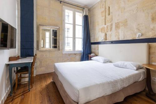 a bedroom with a bed and a desk and a window at Hôtel La Tour Intendance in Bordeaux