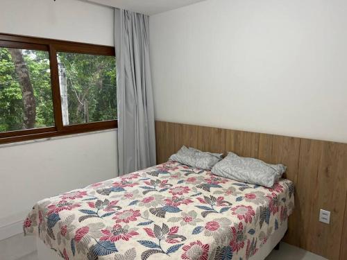 a bedroom with a bed with a floral comforter and a window at Casa 05 suítes, piscina e natureza in Mata de Sao Joao