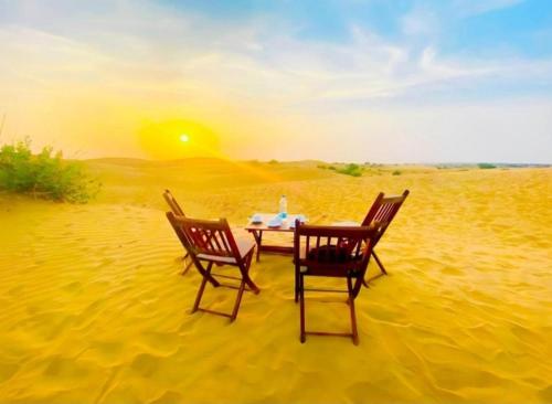 twee stoelen en een tafel in het zand in de woestijn bij Desert Malra Camp in Jaisalmer
