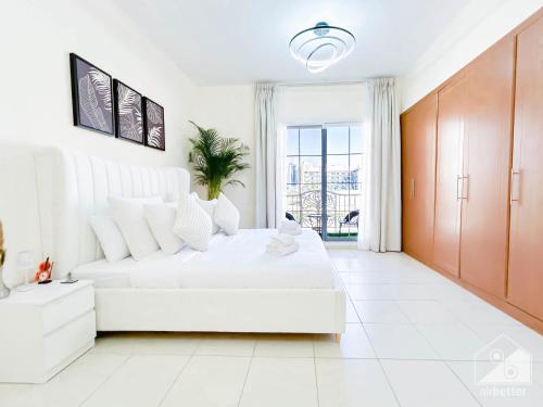 a white bedroom with a large white bed and a window at Gorgeous 1 bedroom with balcony in JVC in Dubai