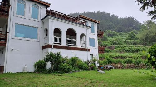 a large white house with a hill in the background at Santa Monica Pension in Kokhae