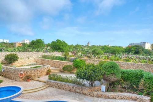 einen Garten mit Büschen und Bäumen und einer Steinmauer in der Unterkunft A lovely 3BR spacious home with Access to POOL by 360 Estates in Qala