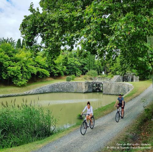 two people riding bikes down a dirt road next to a pond at L'Escale Occitane in Alzonne
