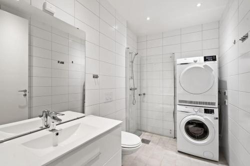 a white bathroom with a washer and dryer in it at Moderne solrik leilighet - gratis lading/sentralt in Kristiansand